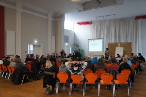 Veranstaltungssaal, Teilnehmer fotografiert von hinten Richtung Bühne