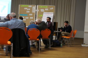 Veranstaltungssaal, Teilnehmer fotografiert von hinten Richtung Bühne